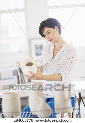 Stock Photograph - Portrait of woman in art studio holding vase and painting it. Fotosearch