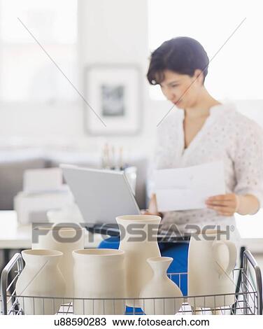 Stock Image - Portrait of woman in art studio using laptop. Fotosearch