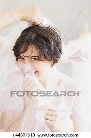 Stock Image - Portrait of woman trying on wedding veil. Fotosearch