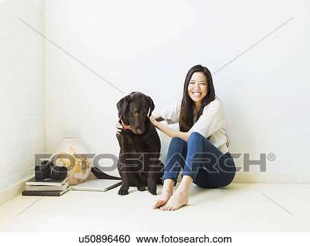 Stock Image - Portrait of woman with dog sitting on floor. Fotosearch