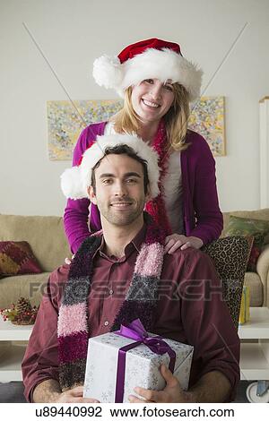 Stock Image - Portrait of young couple wearing santa hats. Fotosearch