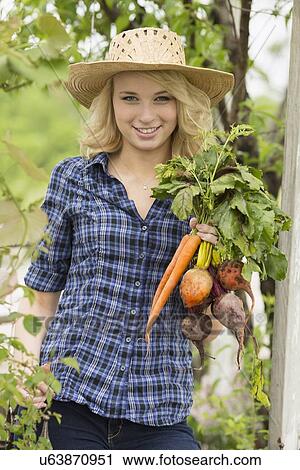 Portrait of young woman holding fresh vegetables in garden View Large Photo Image Stock Image - Portrait of young woman holding fresh vegetables in garden. Fotosearch