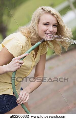 Stock Image - Portrait of young woman holding garden hose. Fotosearch
