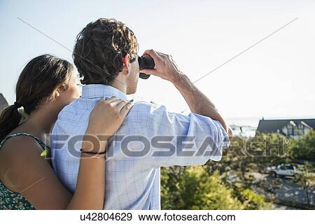 Rear view of couple, man looking through binoculars View Large Photo Image Stock Photo - Rear view of couple, man looking through binoculars. Fotosearch