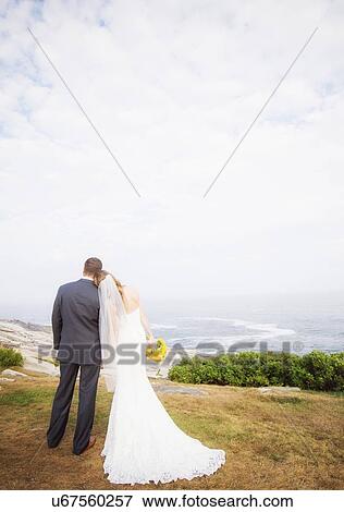 Stock Photo - Rear view of married couple standing by sea. Fotosearch