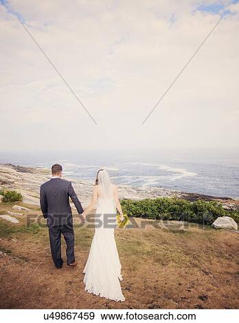 Stock Photo - Rear view of married couple walking by sea. Fotosearch