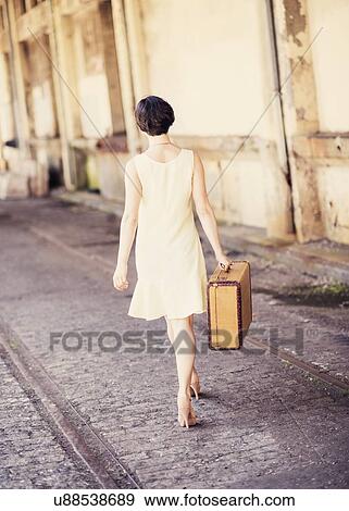 Rear view of woman in dress carrying suitcase at train station View Large Photo Image Stock Photo - Rear view of woman in dress carrying suitcase at train station. Fotosearch