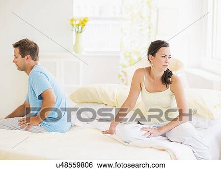 Stock Photograph - Sad couple sitting on bed. Fotosearch