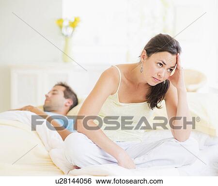 Stock Photograph - Sad woman in bedroom, man sleeping. Fotosearch