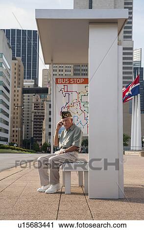 Stock Image - Senior man sitting at bus stop and using mobile phone. Fotosearch