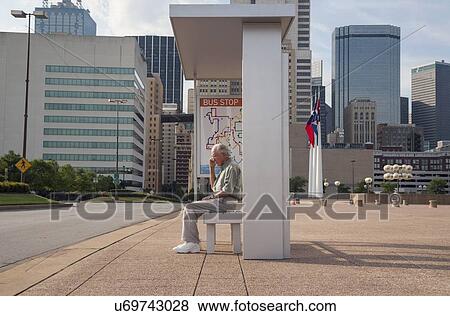 Stock Photo - Senior man sitting at bus stop and using mobile phone. Fotosearch