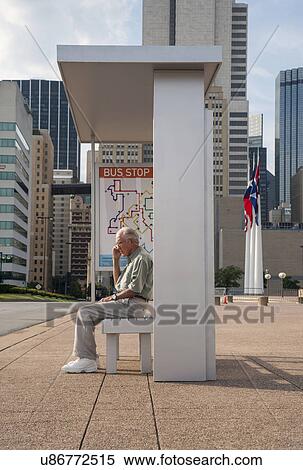 Stock Photography - Senior man sitting at bus stop and using mobile phone. Fotosearch
