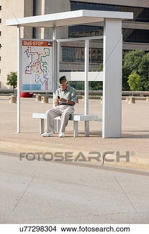 Picture - Senior man sitting at bus stop and text messaging. Fotosearch