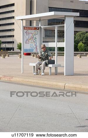 Senior man sitting at bus stop with fishing rod View Large Photo Image Stock Photo - Senior man sitting at bus stop with fishing rod. Fotosearch