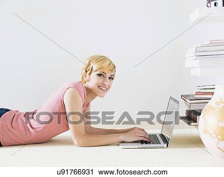 Stock Image - Smiling woman using laptop, studio shot. Fotosearch