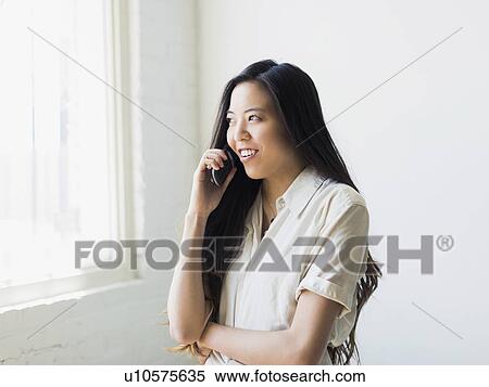 Stock Photography - Smiling young woman talking via mobile phone. Fotosearch