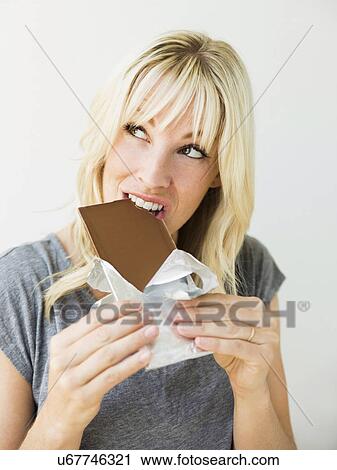 Stock Image - Studio portrait of blonde woman eating chocolate. Fotosearch