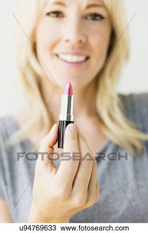 Stock Image - Studio portrait of blonde woman holding pink lipstick. Fotosearch