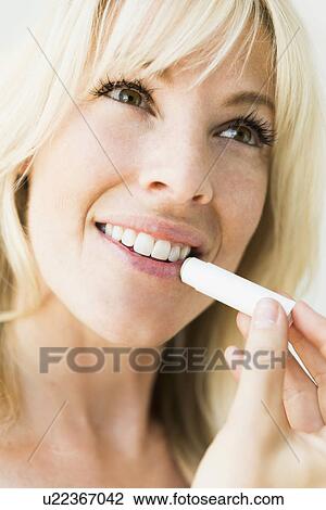 Studio portrait of blonde woman applying lipstick View Large Photo Image Stock Image - Studio portrait of blonde woman applying lipstick. Fotosearch