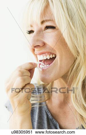 Stock Image - Studio portrait of blonde woman cleaning teeth with dental floss. Fotosearch