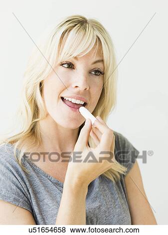 Studio portrait of blonde woman applying lipstick View Large Photo Image Stock Photo - Studio portrait of blonde woman applying lipstick. Fotosearch