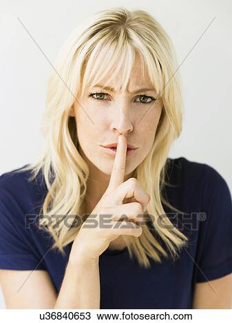 Stock Image - Studio portrait of blonde woman with finger on lips. Fotosearch