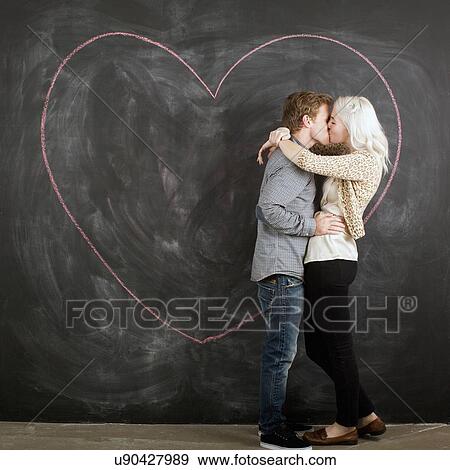 Stock Photo - Studio portrait of young couple embracing in front of blackboard. Fotosearch