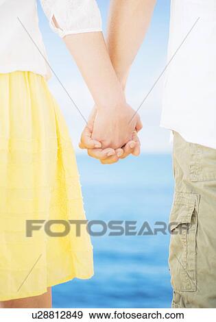 Stock Photo - Studio Shot Mid section of couple standing and holding hands. Fotosearch