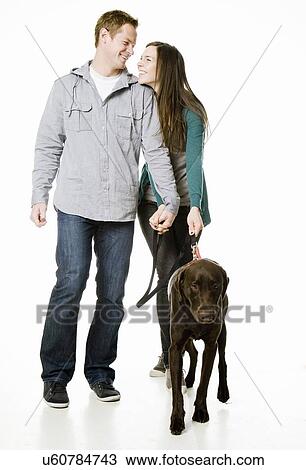 Stock Image - Studio shot of young couple with chocolate labrador. Fotosearch