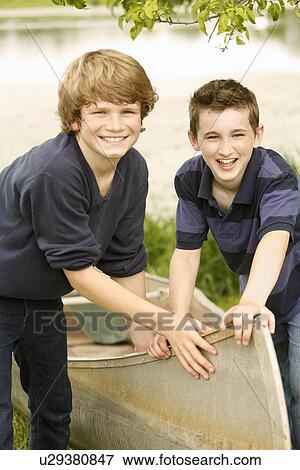 Two boys (12-13) posing with boat on grass near lake View Large Photo Image Stock Photo - Two boys (12-13) posing with boat on grass near lake. Fotosearch