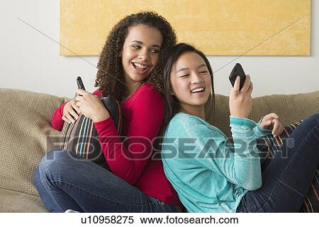 Two friends (12-13, 16-17) sitting on sofa and playing with smartphone View Large Photo Image Stock Photography - Two friends (12-13, 16-17) sitting on sofa and playing with smartphone. Fotosearch
