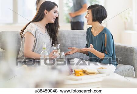 Stock Photo - Two friends sitting on sofa and talking. Fotosearch