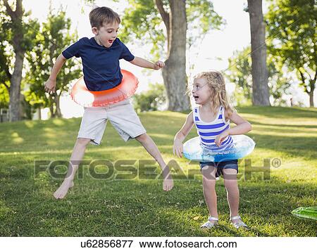 Stock Photo - Two kids (4-5, 6-7) playing with inflatable rings in park . Fotosearch
