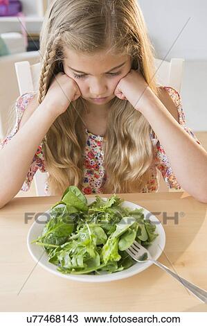 Stock Image - View of unhappy girl (8-9) with salad. Fotosearch