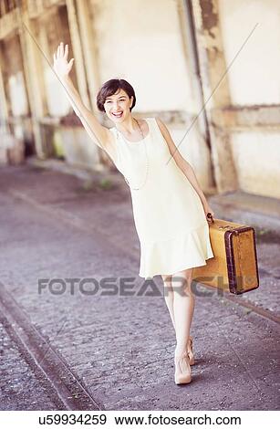 Woman in dress holding suitcase at train station, waving hand View Large Photo Image Stock Photo - Woman in dress holding suitcase at train station, waving hand. Fotosearch