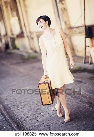 Stock Photography - Woman in dress holding suitcase at train station. Fotosearch