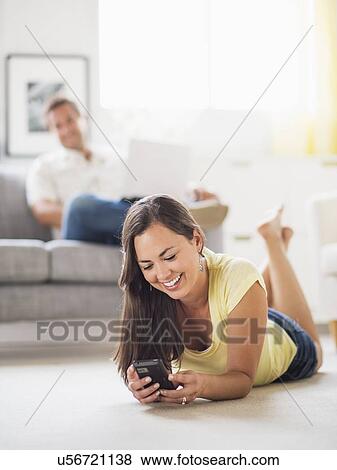 Woman lying on front and using mobile phone, man in background View Large Photo Image Stock Photo - Woman lying on front and using mobile phone, man in background. Fotosearch