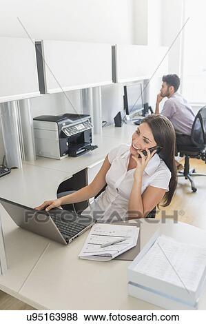 Stock Photo - Woman talking on cell phone in office. Fotosearch