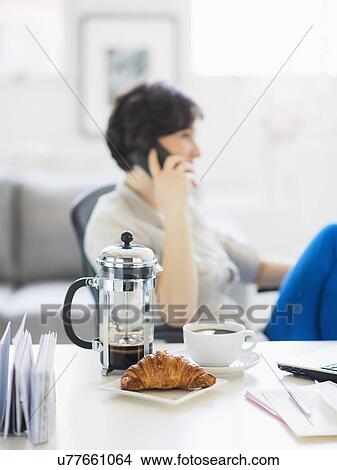 Picture - Woman talking on phone, coffee and croissant in foreground. Fotosearch