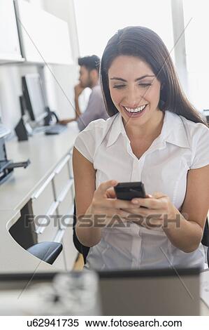 Woman text messaging in office, man in background View Large Photo Image Stock Photography - Woman text messaging in office, man in background. Fotosearch