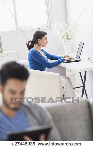 Stock Photography - Woman using laptop and man using digital tablet at home. Fotosearch