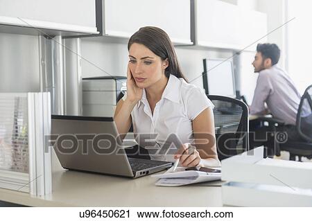 Stock Image - Woman working in office, man in background. Fotosearch