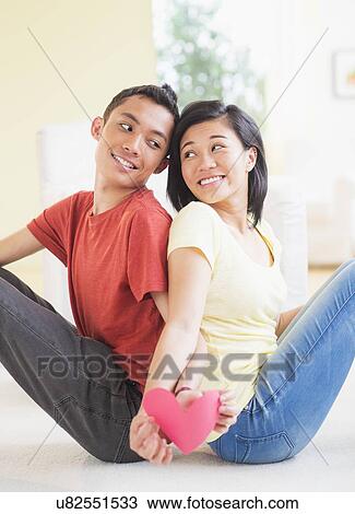 Young couple sitting back to back holding paper heart View Large Photo Image Stock Image - Young couple sitting back to back holding paper heart. Fotosearch