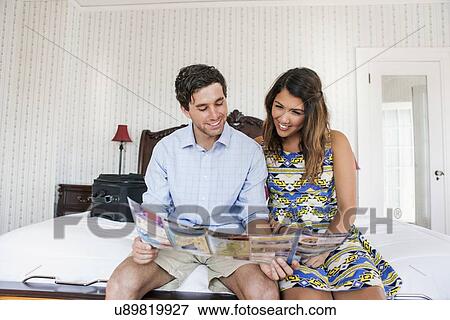 Stock Photo - Young couple sitting on bed in hotel room and reading brochure. Fotosearch
