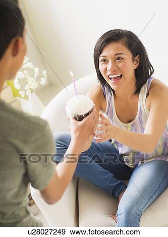 Young man giving cupcake with candle to woman View Large Photo Image Stock Photo - Young man giving cupcake with candle to woman. Fotosearch