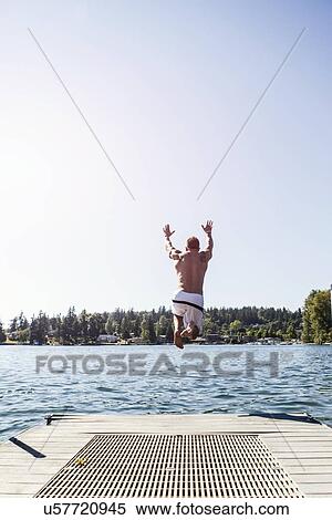 Stock Photography - Young man jumping to lake from jetty. Fotosearch