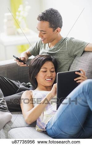 Young people using mobile phone and digital tablet on sofa View Large Photo Image Stock Photograph - Young people using mobile phone and digital tablet on sofa. Fotosearch