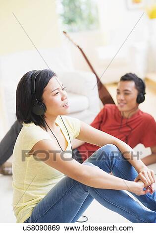 Stock Photo - Young woman and man listening music with headphones on. Fotosearch