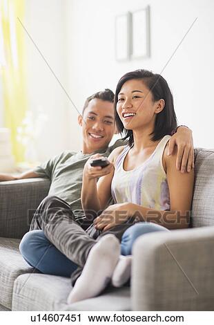 Stock Image - Young woman and young man sitting on sofa. Fotosearch