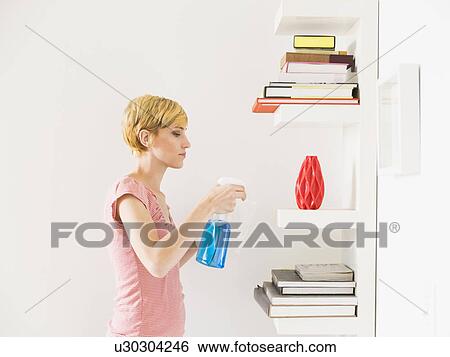 Stock Photograph - Young woman cleaning bookshelf. Fotosearch